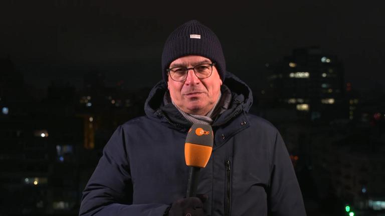 ZDF-Reporter Henner Hebestreit vor dunklem Hintergrund mit Mikrofon