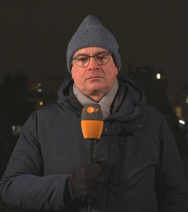 Henner Hebestreit mit Mikrofon, Mütze und Winterjacke