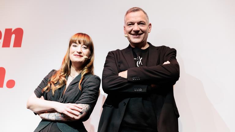 Heidi Reichinnek und Jan van Aken stehen mit verschränkten Armen nebeneinander.