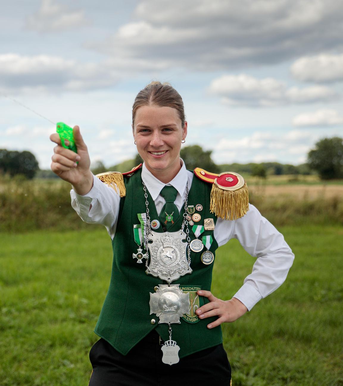 Anneke steht mit einer Wasserspritzpistole in der Hand auf einem Feld und drückt ab.