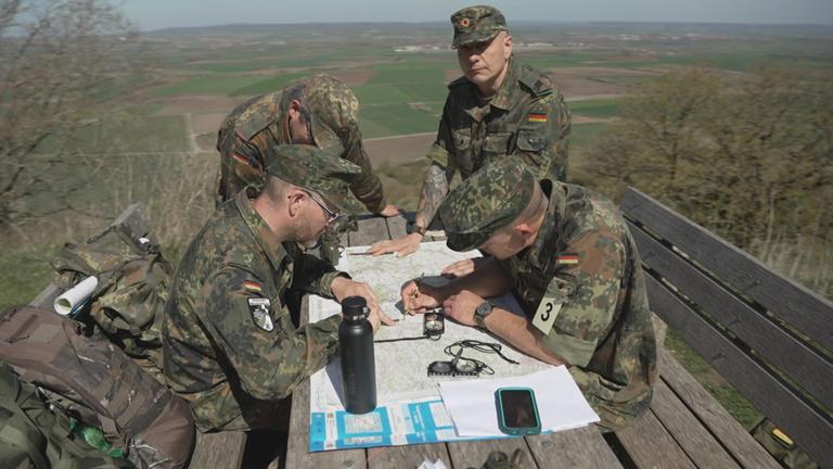 Reservisten sitzen um einen Tisch und haben eine Karte und einen Kompass vor sich. Sie üben die Orientierung im Gelände.