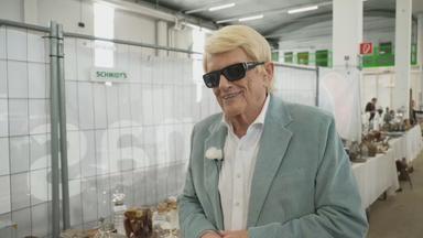 Das Bild zeigt Schlagersänger Heino in einer Lagerhalle mit den Gegenständen, die er versteigern wird.