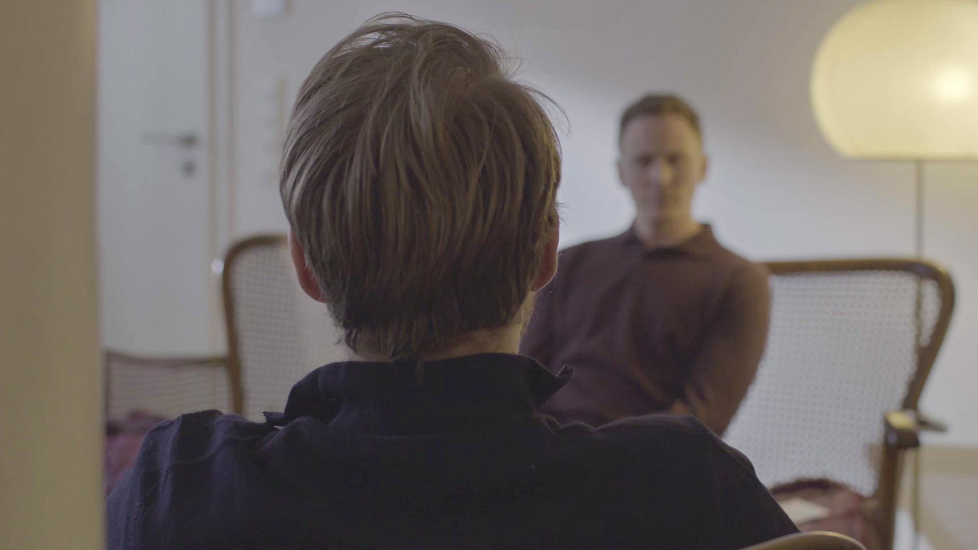 Heinrich XXVII. Prinz Reuß sitzt mit dem Rücken zur Kamera. Im Hintergrund ist Jochen Breyer unscharf zu sehen, der den Sohn von Prinz Reuß interviewt.