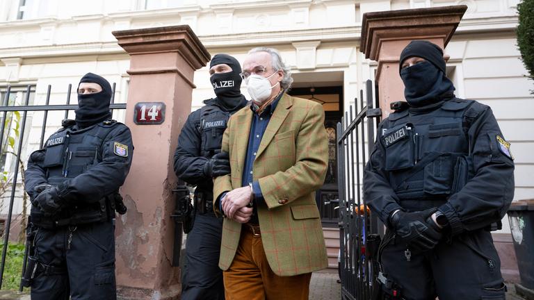 Polizisten führen Heinrich XIII. Prinz Reuß (2.v.r.) nach der Durchsuchung eines Hauses zu einem Polizeifahrzeug