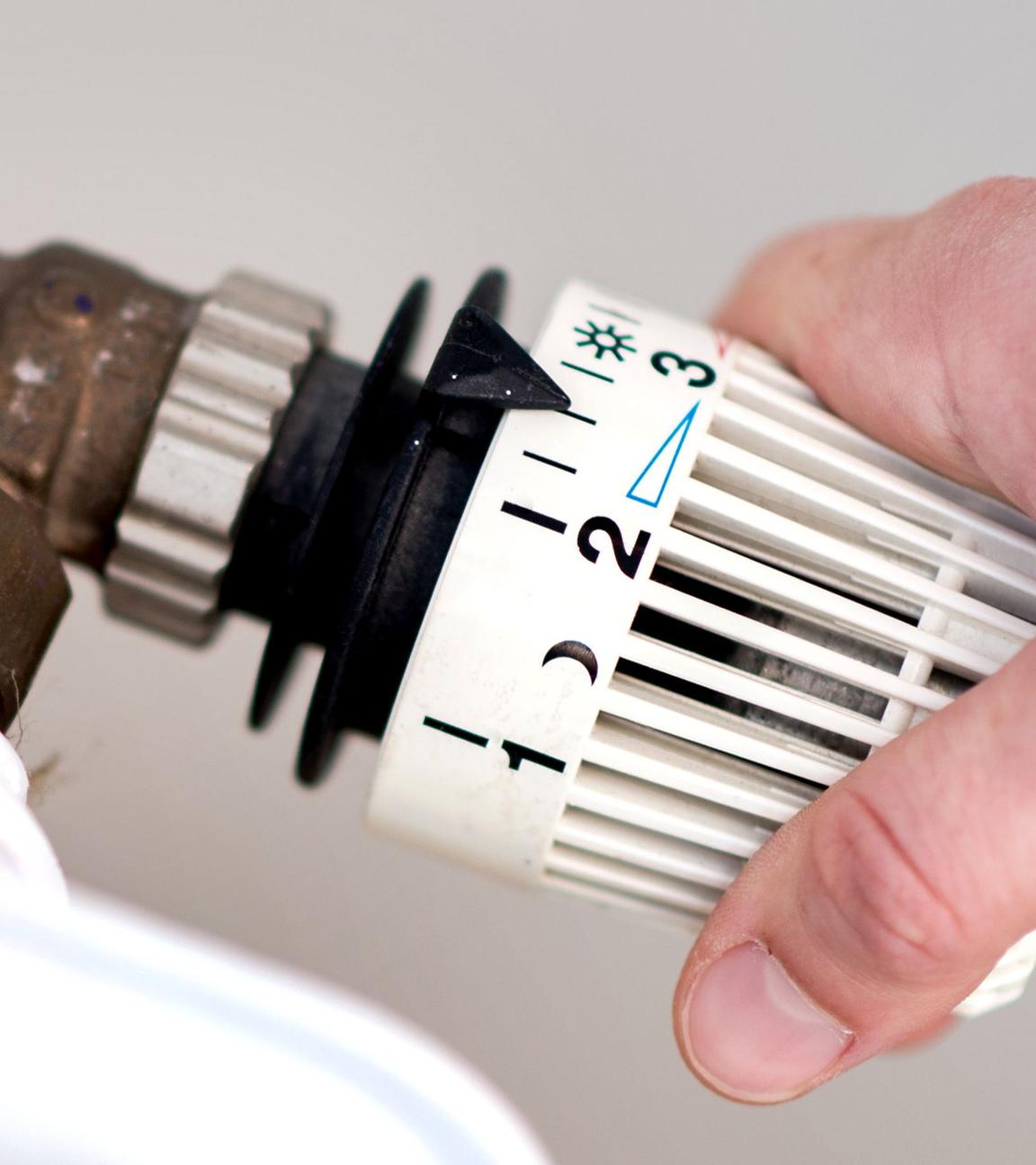Eine Frau dreht am Thermostat einer Heizung. (Symbolbild)
