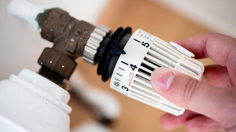 Eine Frau dreht am Thermostat einer Heizung. (Archivbild)