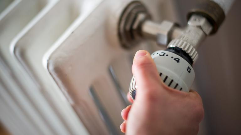 EIne Hand dreht an einem Heizungsregler.