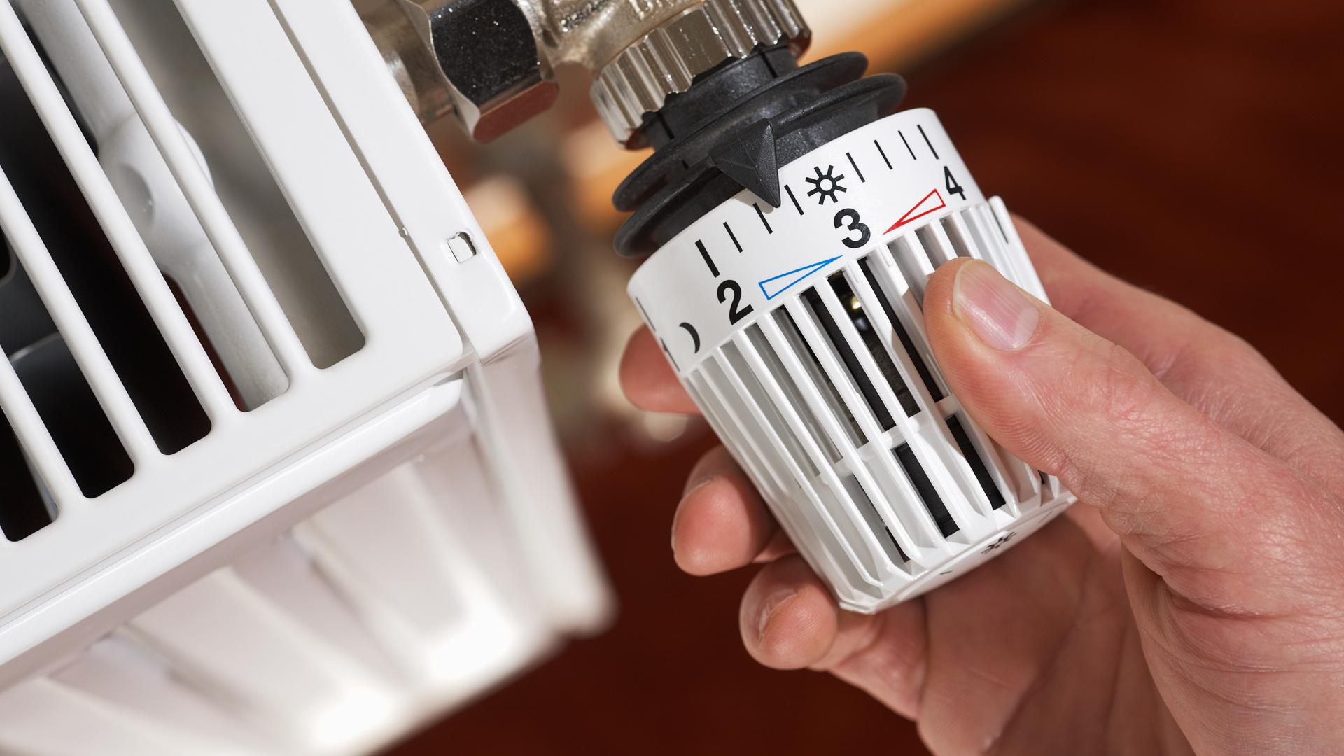 Heizen bleibt teuer: Eine Hand dreht am Temperaturregler einer Heizung.