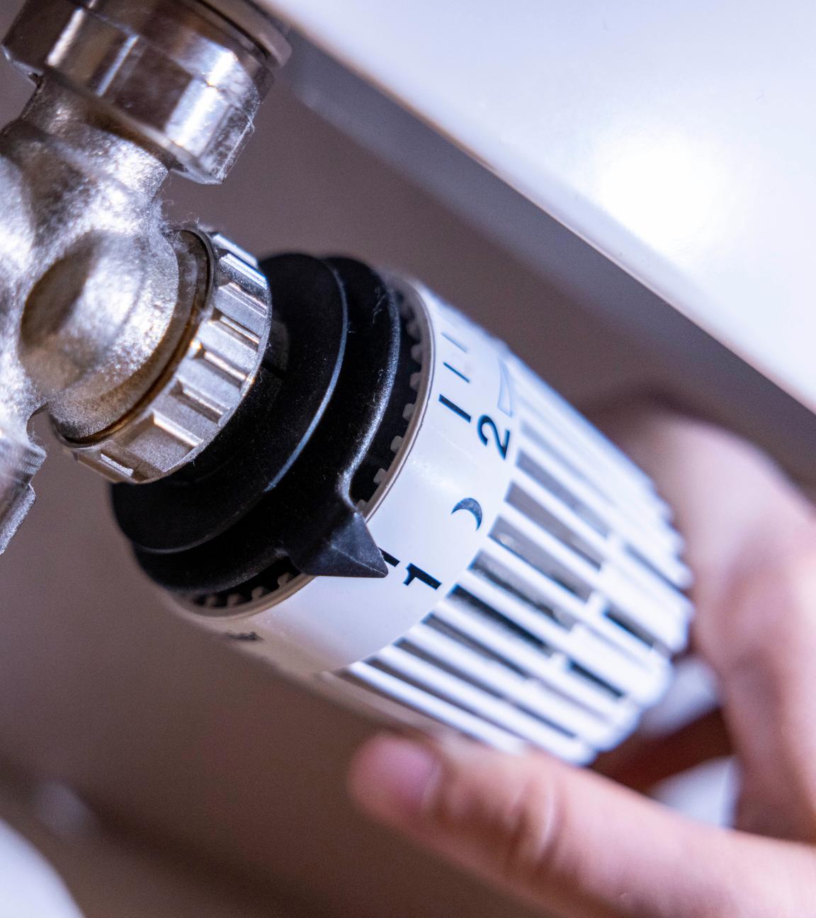 Eine Person dreht am Thermostat einer Heizung.