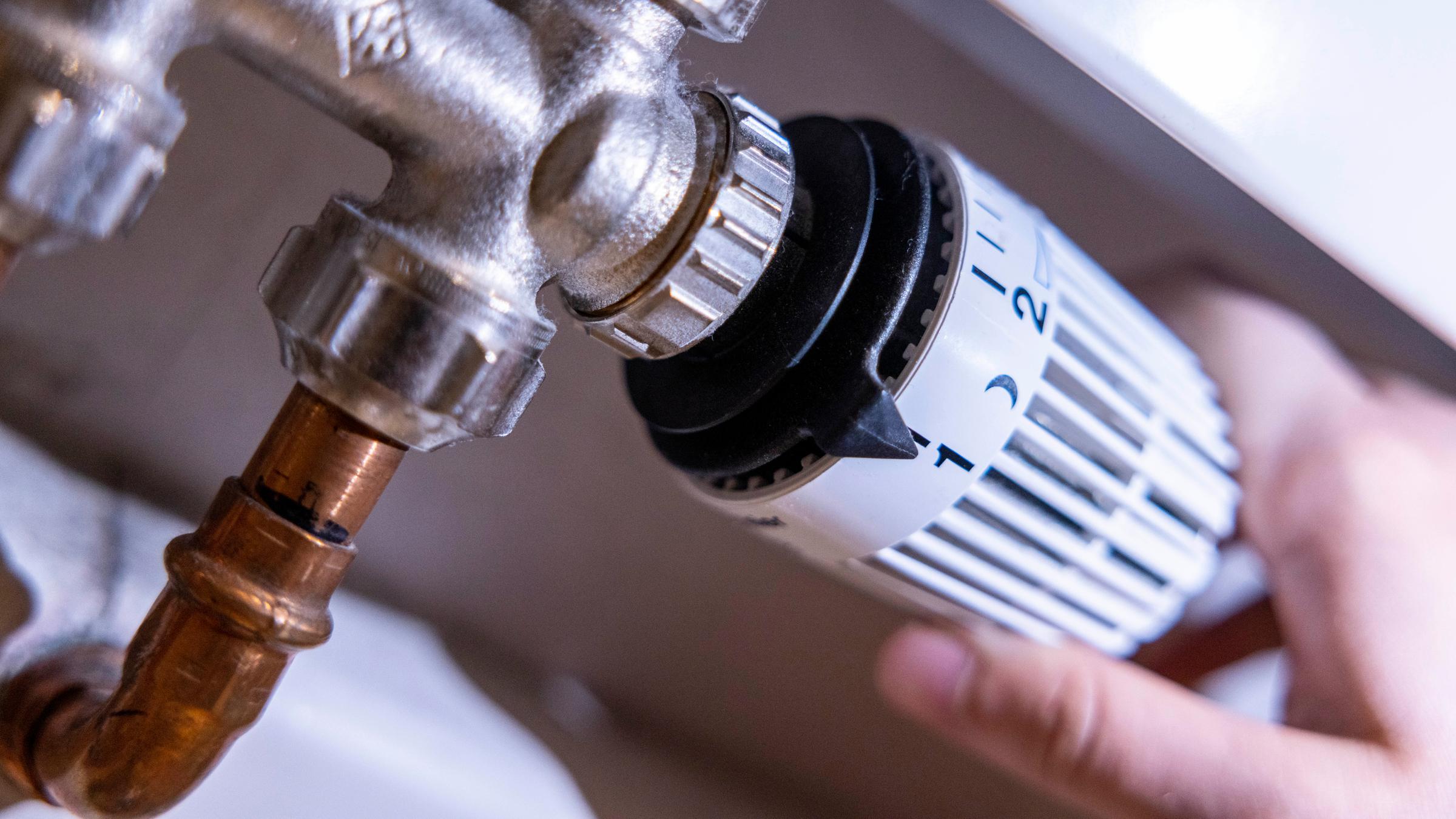 Eine Person dreht am Thermostat einer Heizung.