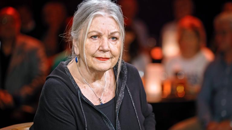 Porträtfoto einer älteren Frau mit zurückgebundenen langen grauen Haaren.