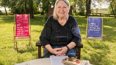 Eine Frau mit grauen Haaren sitzt im Freien und lächelt.