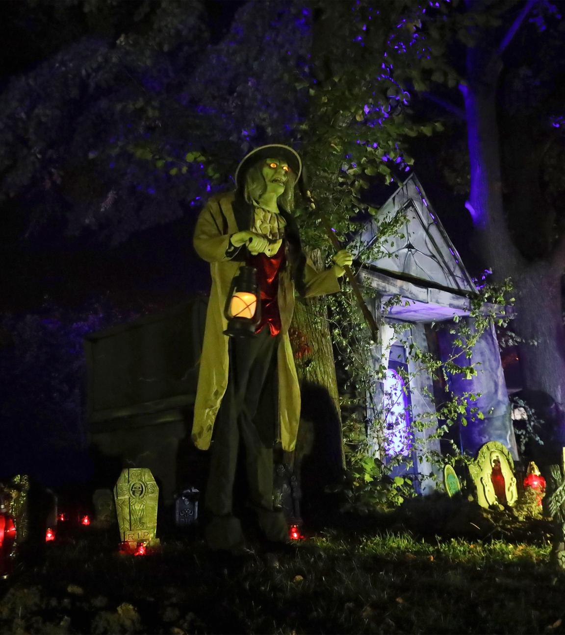 Helloween-Deko mit Geistern, Grabsteinen und einer Person mit Lampe