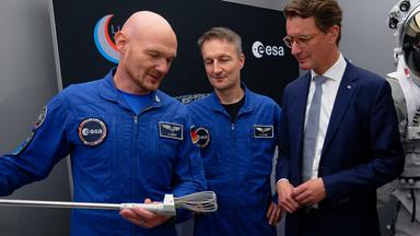 Die Astronauten Matthias Maurer und Alexander Gerst (l) und der nordrhein-westfälische Ministerpräsident Hendrik Wüst (r, CDU) betrachten bei einem Besuch des neuen FLEXhab und der Mondsimulationsanlage LUNA am Deutschen Zentrum für Luft- und Raumfahrt (DLR) und der European Space Agency (ESA) ein Werkzeug zum Aufheben von Mondgestein. 