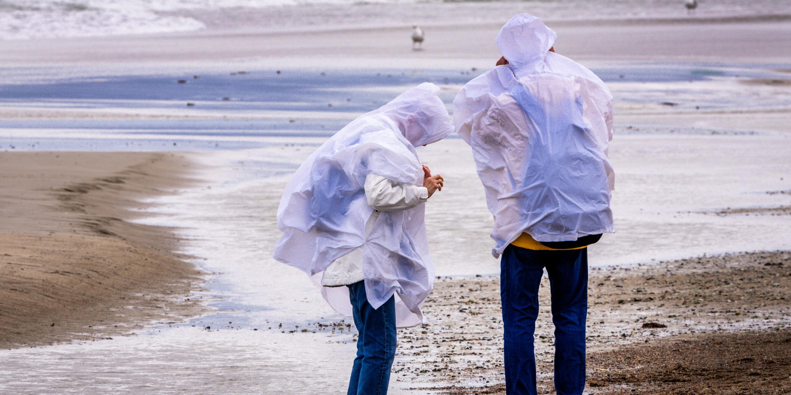 Spaziergänger mit Regenschutz suchen bei kräftigem Wind am Ostseestrand von Warnemünde nach Bernstein.