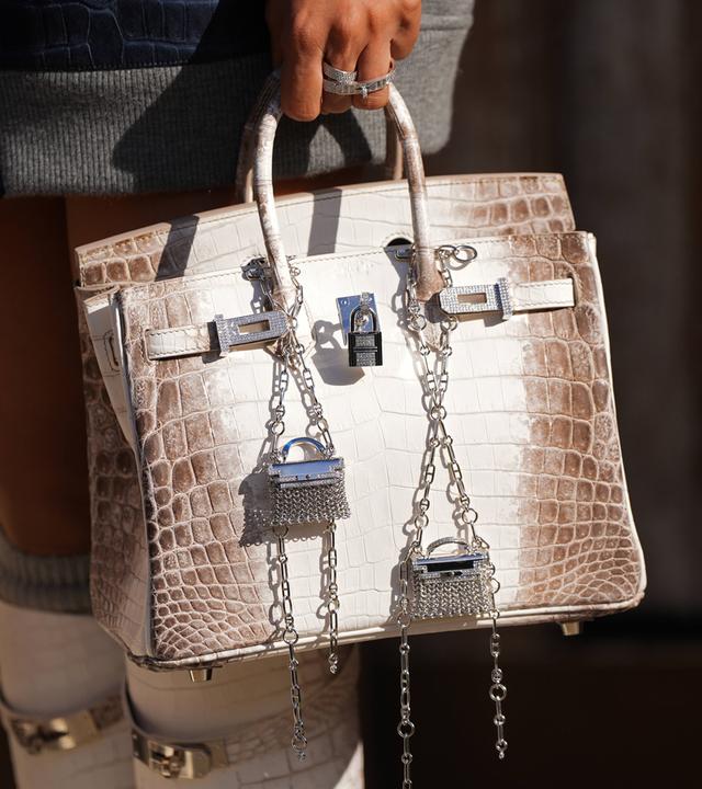Eine Frau trägt eine Birkin-Handtasche von Hermès aus weißem Krokodilleder.