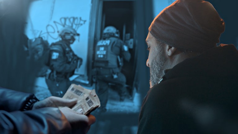 Im Hintergrund sind Polizisten in voller Ausrüstung zu sehen, die offenbar ein Haus stürmen. Im Vordergrund ist rechts ein Mann mit Bart und Mütze zu sehen. Links daneben sieht man die Hände eines anderen Mannes, der 50 Euro-Scheine hält.