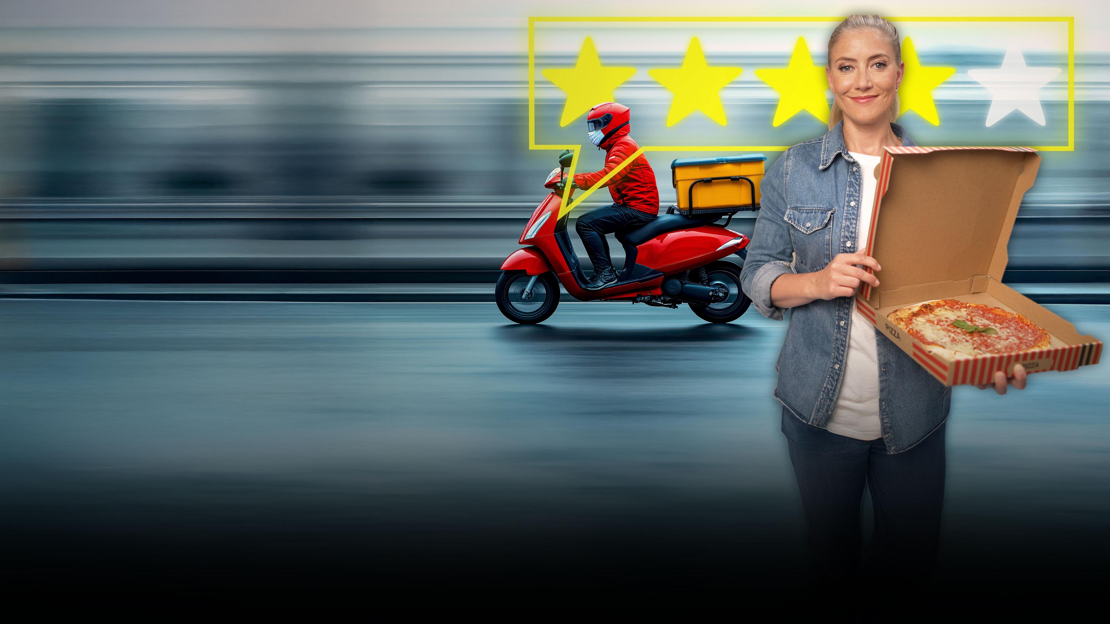 Pia Osterhaus steht in einer Großküche und hält eine fertige Pizza im Karton in der Hand. Sie schaut lächelnd in die Kamera. Im Hintergrund Im Hintergrund fährt ein Mopedfahrer mit Lieferung.  