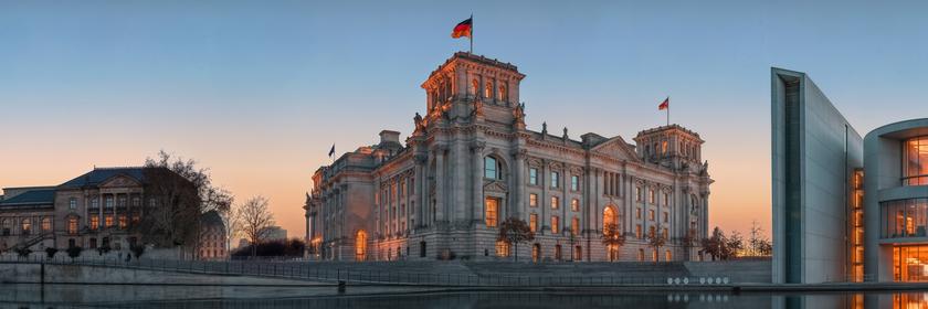 Der Bundestag im Sonnenuntergangslicht. Rechts vom Reichstag ist noch ein Teil des Paul-Löbe-Hauses zu erkennen. Links andere Gebäude im politischen Berlin. Alle Gebäude spiegeln sich am unteren Bildrand in der Spree.