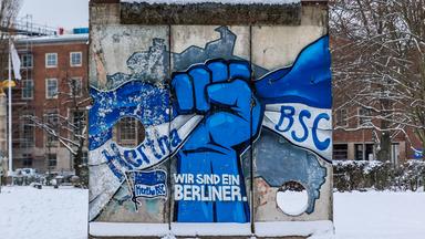 Ein Mauerstück mit einem Grafitto und dem Schriftzug «Wir sind ein Berliner» steht vor der Geschäftsstelle des Fußball-Zweitligisten Hertha BSC