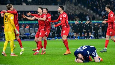 Pascal Klemens (Hertha) kniet am Boden und versteckt sein Gesicht, während Freiburger Spieler jubeln.