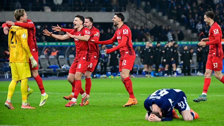 Pascal Klemens (Hertha) kniet am Boden und versteckt sein Gesicht, während Freiburger Spieler jubeln.
