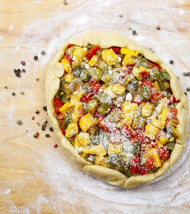 Herzhaft belegte Galette auf mehliertem Holzbrett.