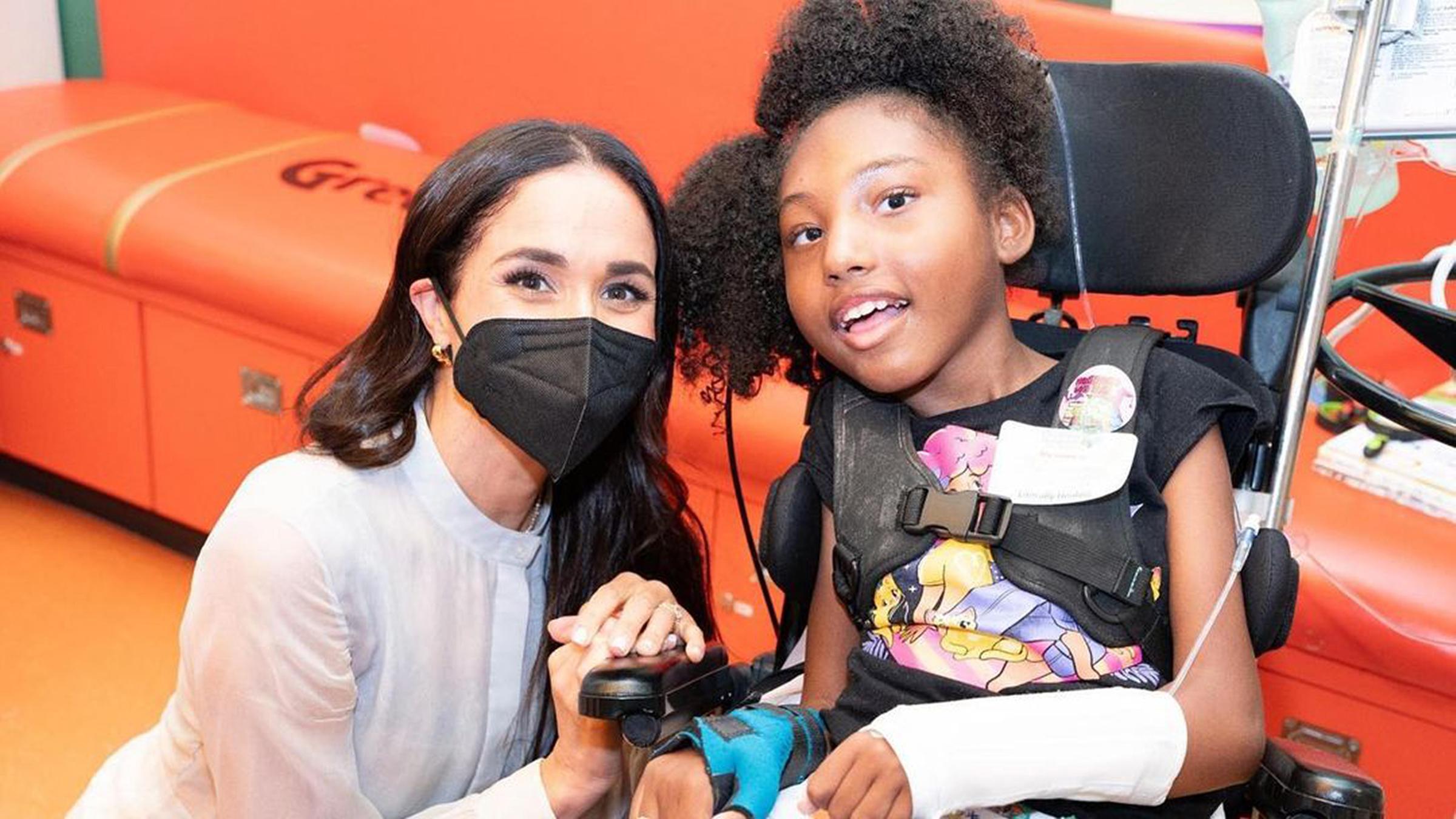 Herzogin Meghan mit einer FFP-Maske neben einem Kind im Rollstuhl