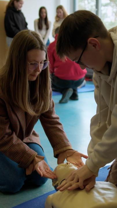 Expertin für "Herzsicherheit an Schulen": Liliane Kozik (links) zeigt einem Schüler (rechts) Reanimationsmaßnahmen an einem Dummy der auf dem Boden liegt.