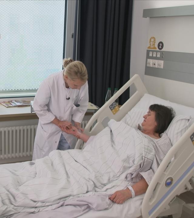 Frau liegt im Krankenhausbett im Frauenherzzentrum Frankfurt und zwei Ärztinnen stehen neben dem Bett.