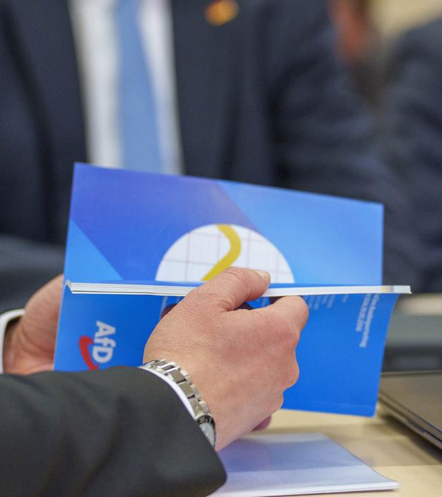  Im Vordergrund blättert ein AfD-Vertreter im Programm für Deutschland der AfD.