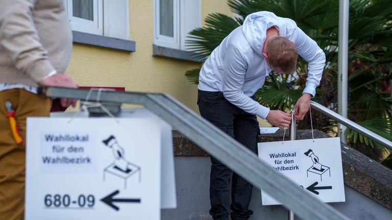 Ein Mann befestigt ein Hinweisschild zu einem Wahllokal an einem Treppenaufgang