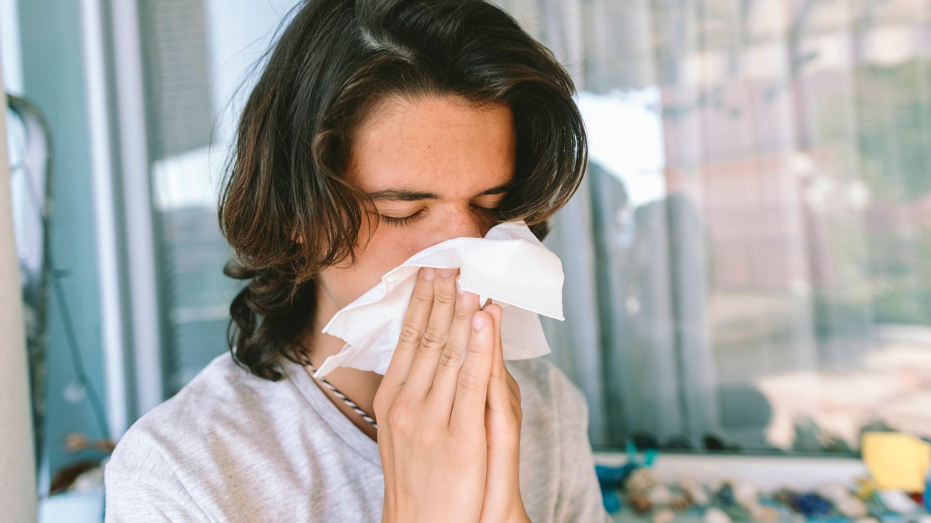 Ein junger Mann mit dunklen Haaren niest in ein Taschentuch.