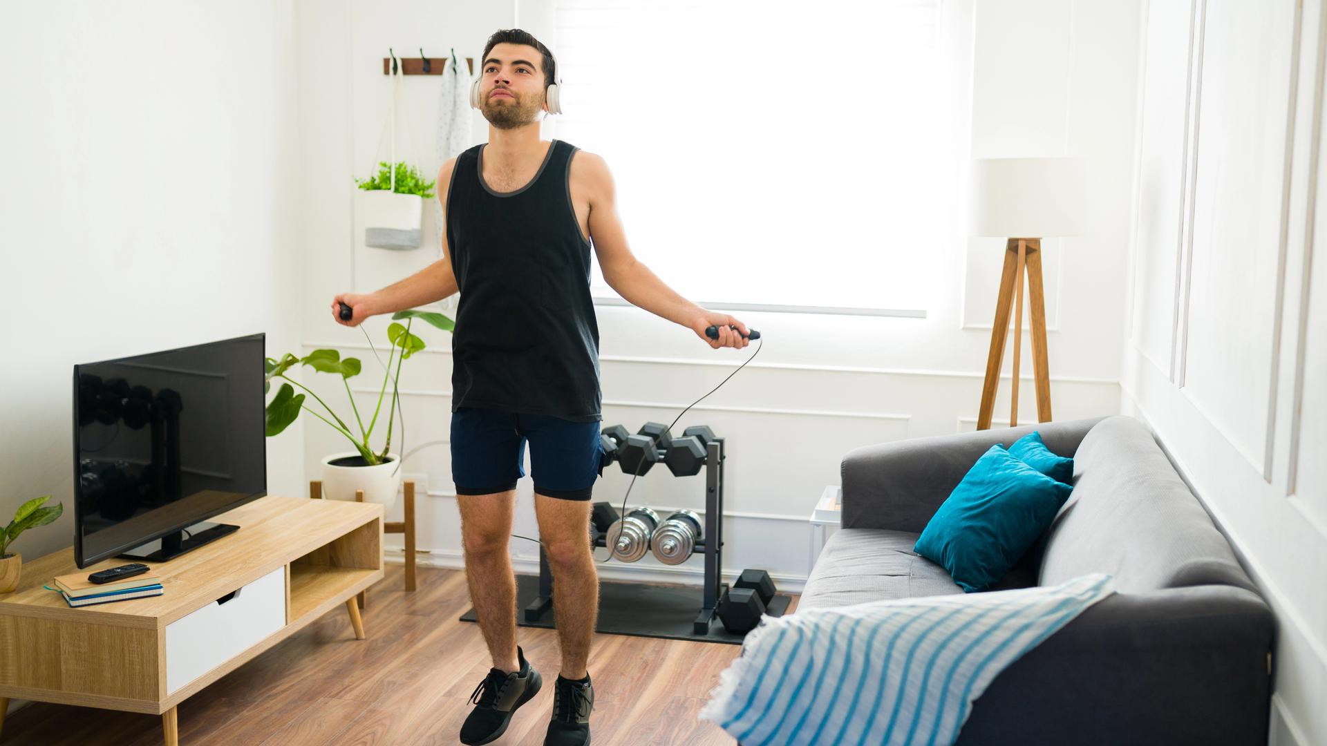 Ein Mann trainiert mit Seilhüpfen im eigenen Wohnzimmer.