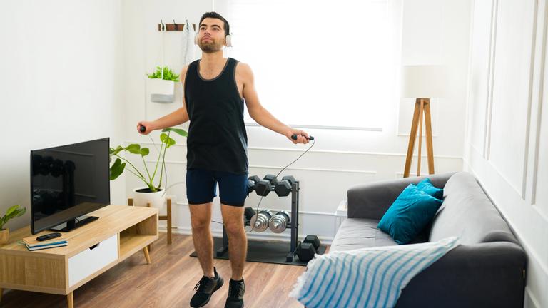 Ein Mann trainiert mit Seilhüpfen im eigenen Wohnzimmer.