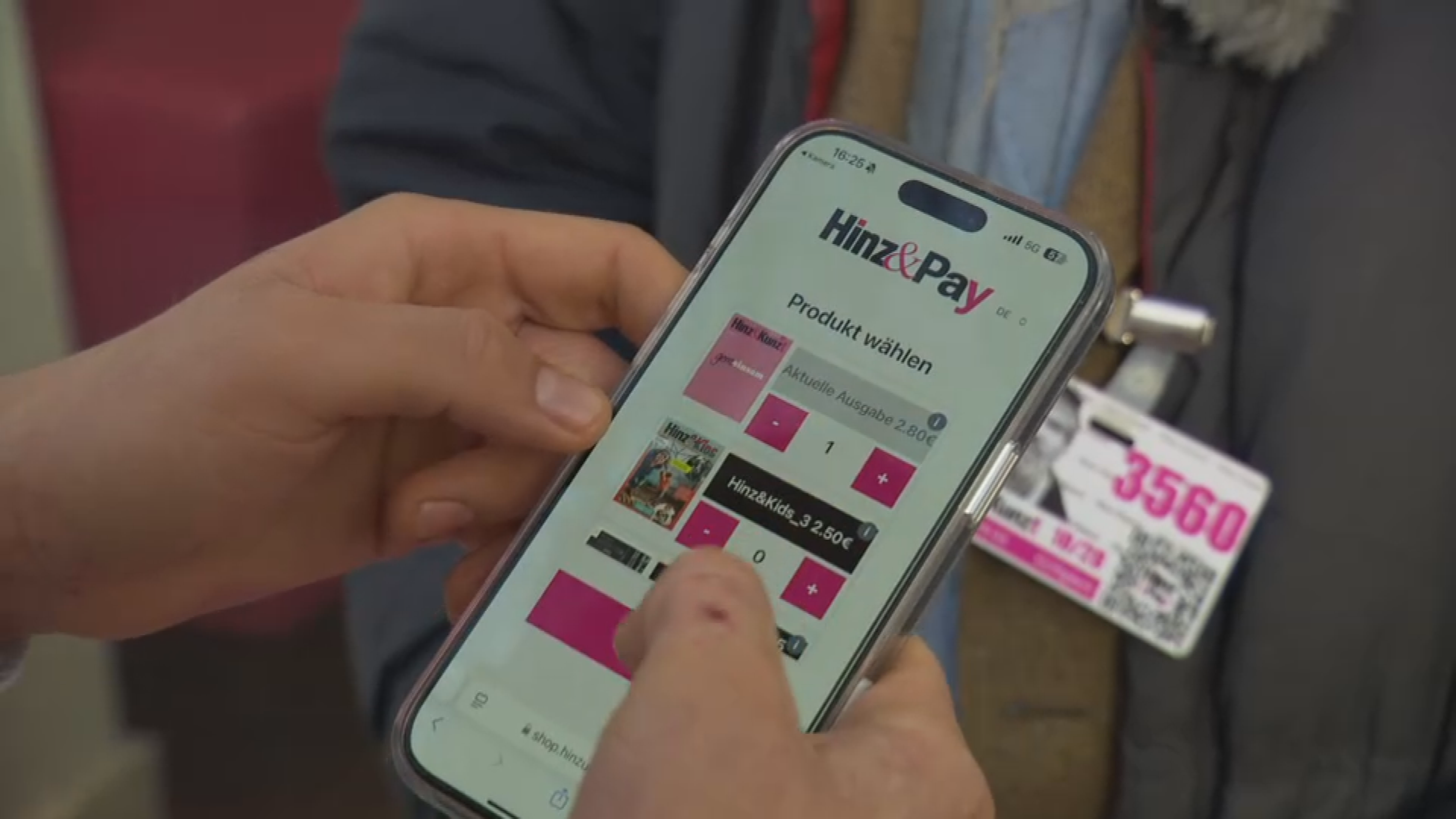 Ein Handy scannt den Ausweis eines Verkäufers der Straßenzeitung Hinz&Kunzt und wählt ein Produkt auf dem Bildschirm aus.