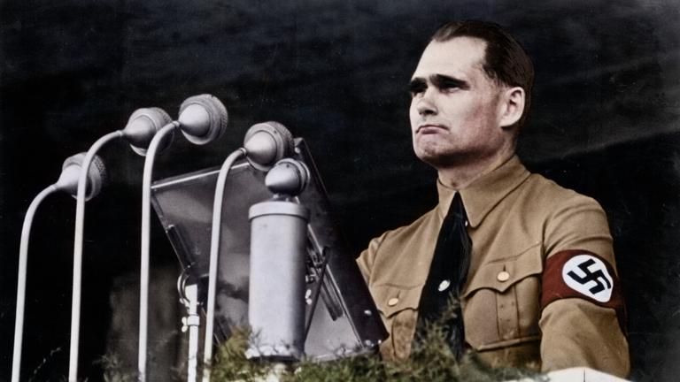Hitlers Stellvertreter Rudolf Hess steht in brauner Parteiuniform am Rednerpult.