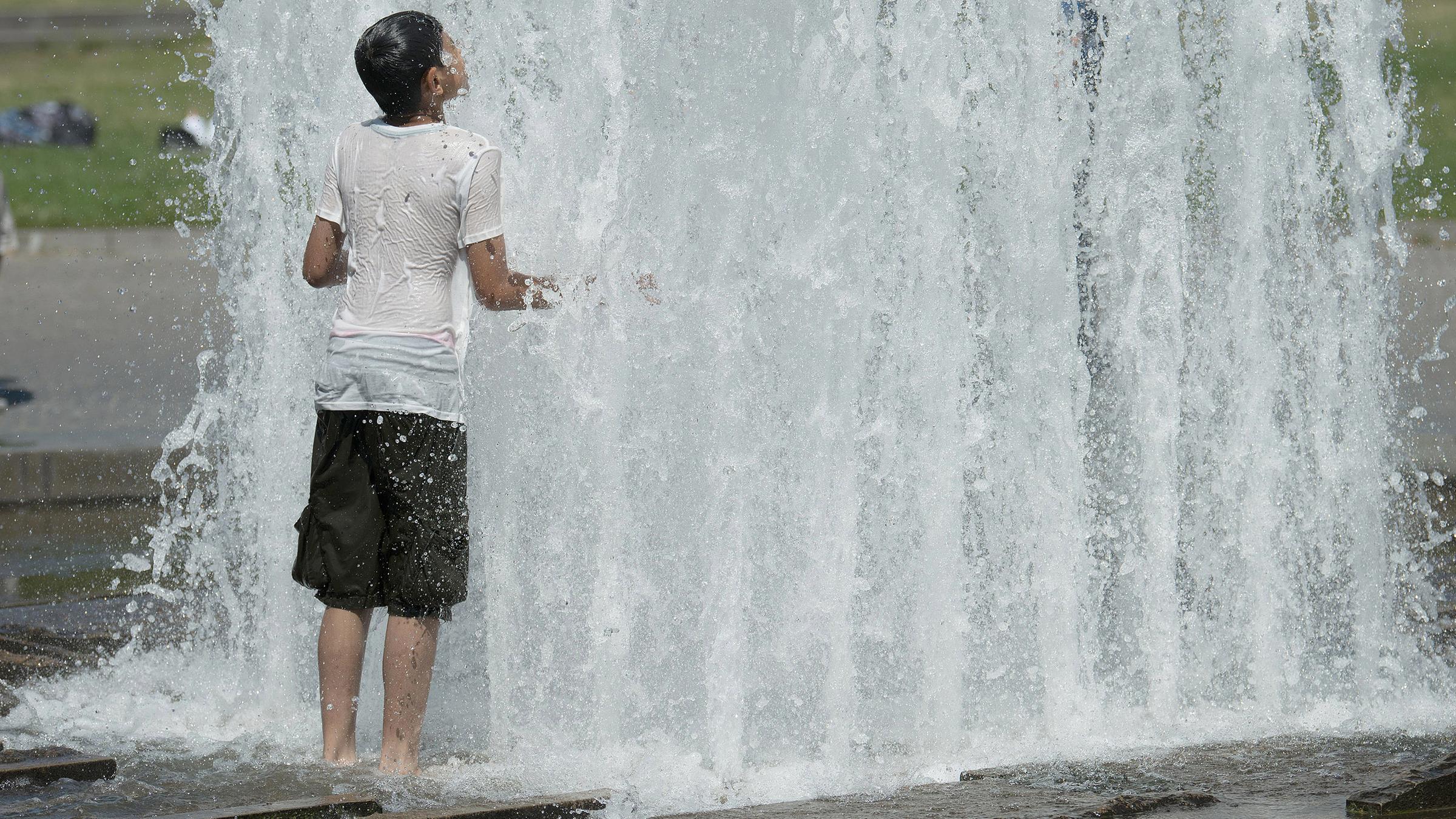 Ein Jugendlicher erfrischt sich mit einem Bad in einem Brunnen, am 24.07.2019 in Berlin.