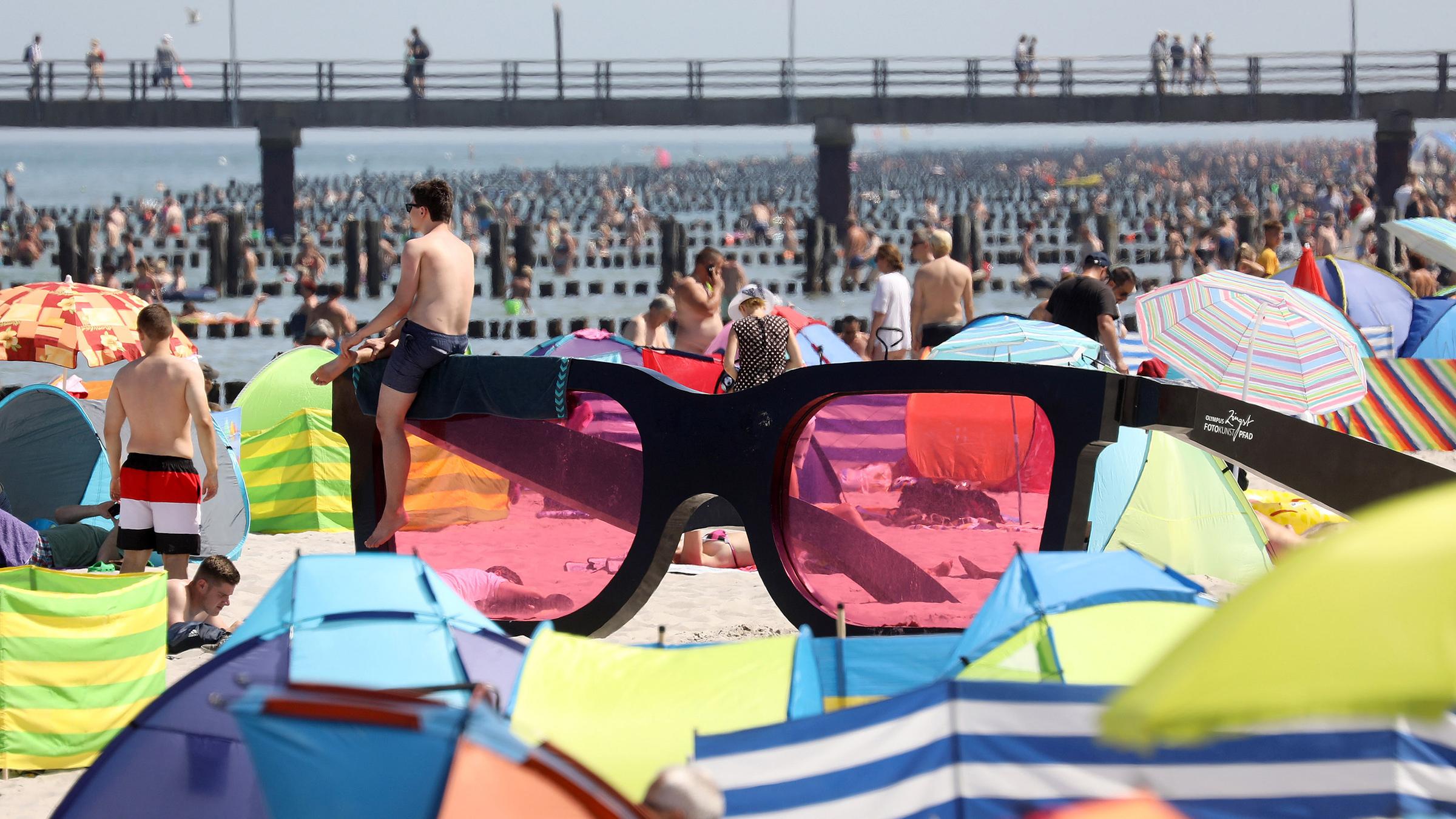 Badegäste liegen am Strand rund um eine große rosarote Brille, am 24.07.2019 in Zingst.