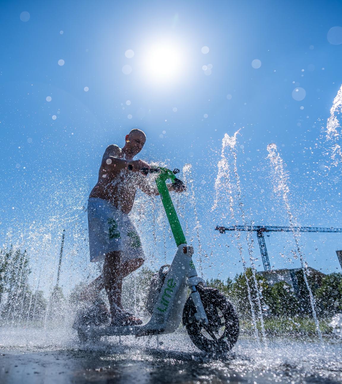 Tomas aus Berlin fährt mit seinem E-Scooter durch das Wasserspiel vor dem Kanzleramt.