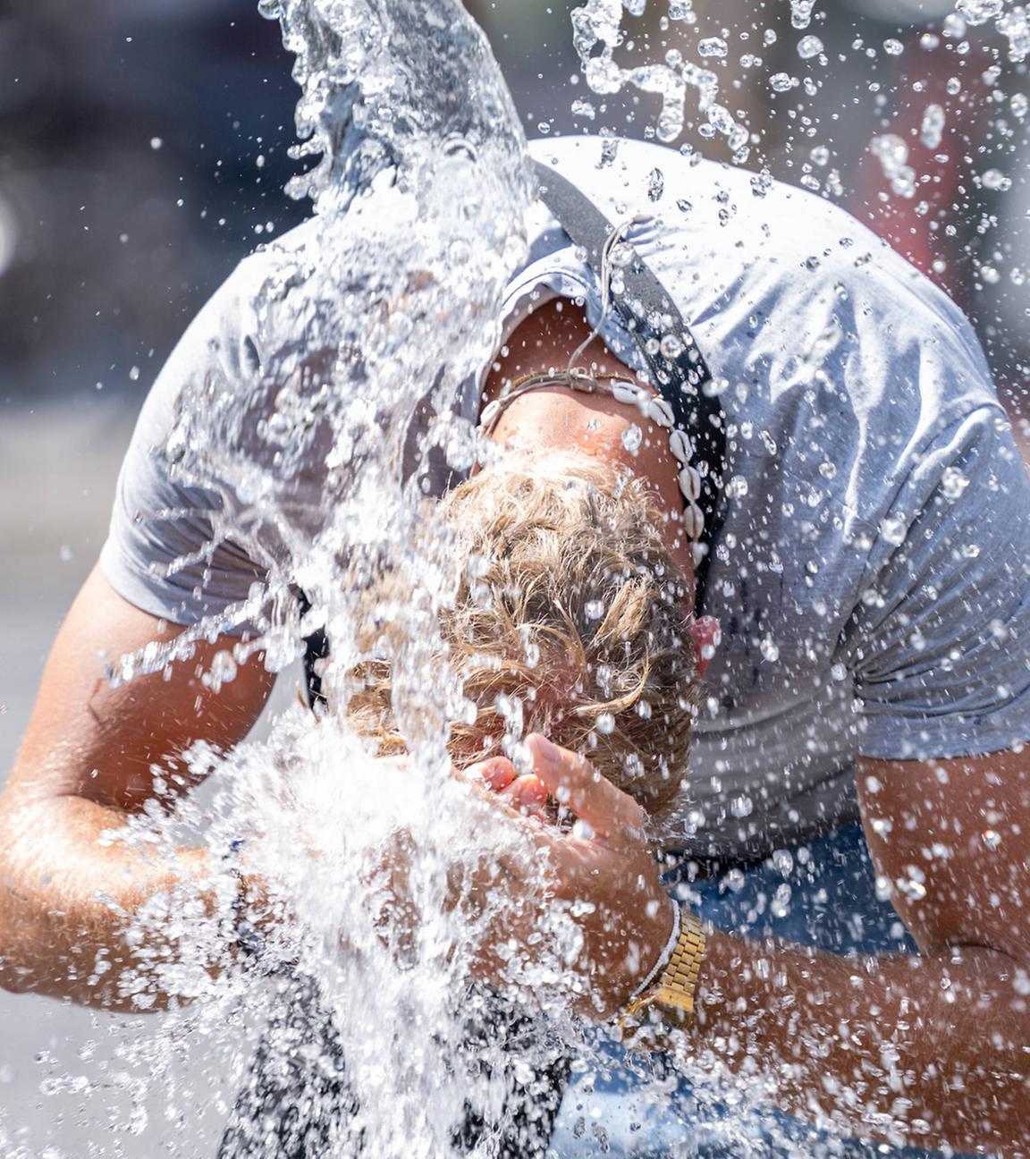 Bei heißen Temperaturen erfrischt sich ein Mann in den Wasserfontänen in der Frankfurter Innenstadt.