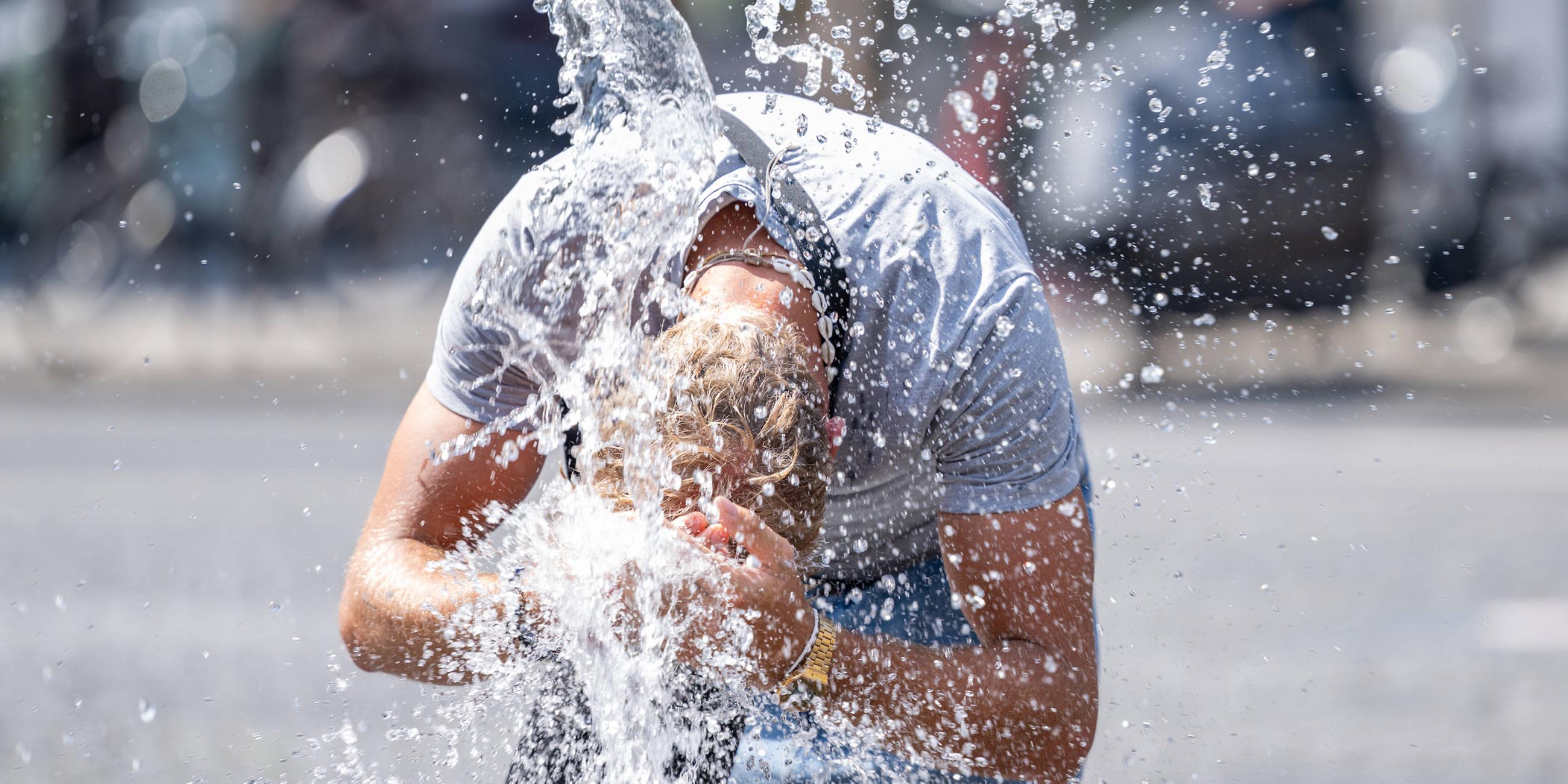 Bei heißen Temperaturen erfrischt sich ein Mann in den Wasserfontänen in der Frankfurter Innenstadt.