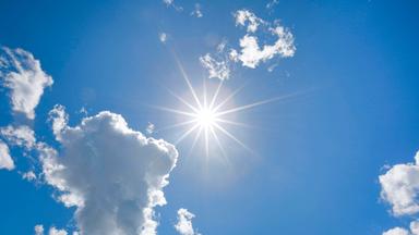 Symbolbild: Sonne am blauen Himmel mit einigen Quellwolken im Gegenlicht