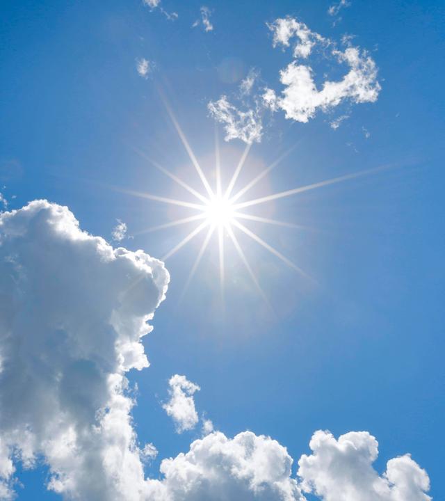 Symbolbild: Sonne am blauen Himmel mit einigen Quellwolken im Gegenlicht