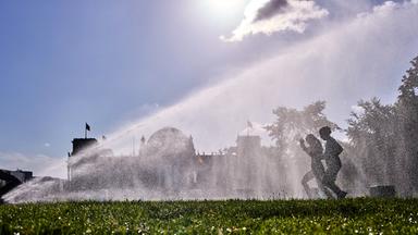 Frauen laufen an einem Sprinkler vor dem Reichstagsgebäude in Berlin an einem Sommermorgen vorbei, aufgenommen am 11.08.2026