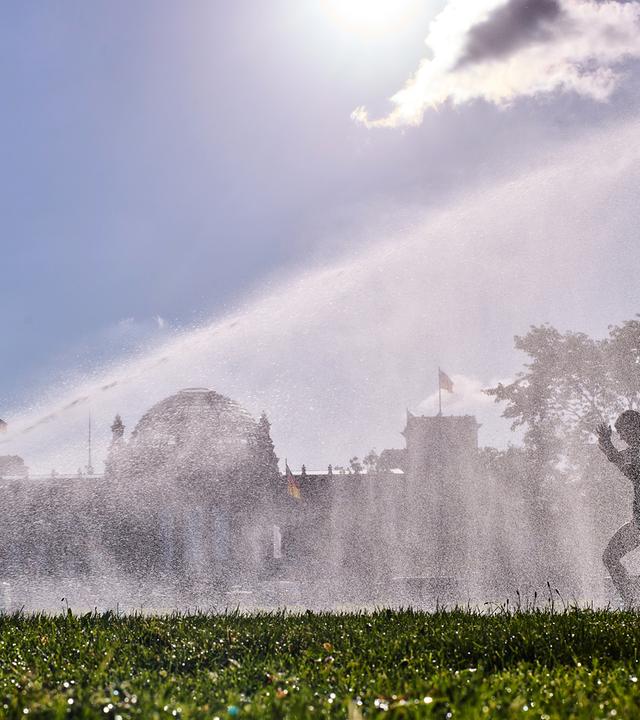 Frauen laufen an einem Sprinkler vor dem Reichstagsgebäude in Berlin an einem Sommermorgen vorbei, aufgenommen am 11.08.2026