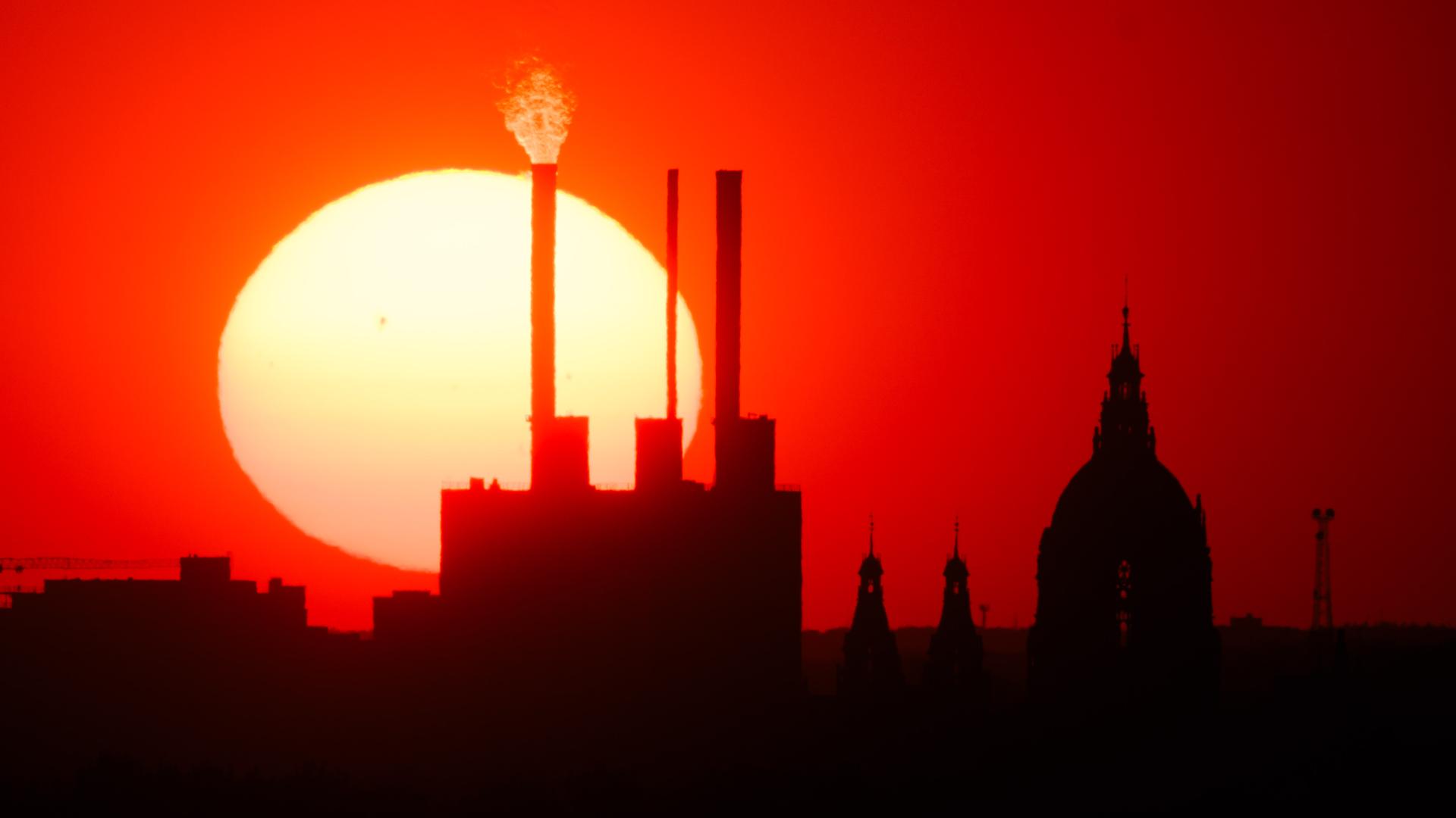Die Sonne geht hinter dem Heizkraftwerk Linden und dem Neuen Rathaus unter. 