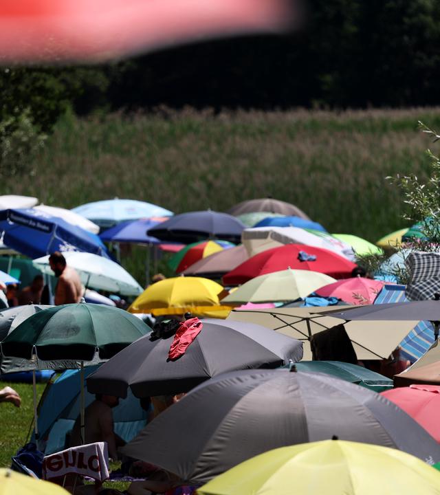 Menschen suchen Abkühlung unter Sonnenschirmen am Ufer des am Alpenrand gelegenen Illasbergsees. 