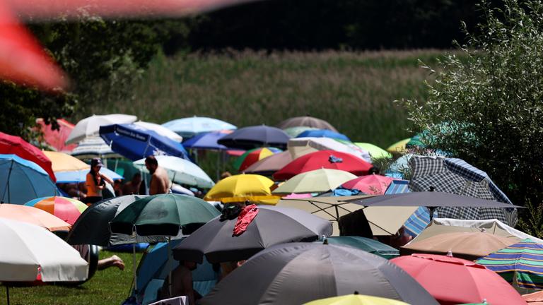Menschen suchen Abkühlung unter Sonnenschirmen am Ufer des am Alpenrand gelegenen Illasbergsees. 