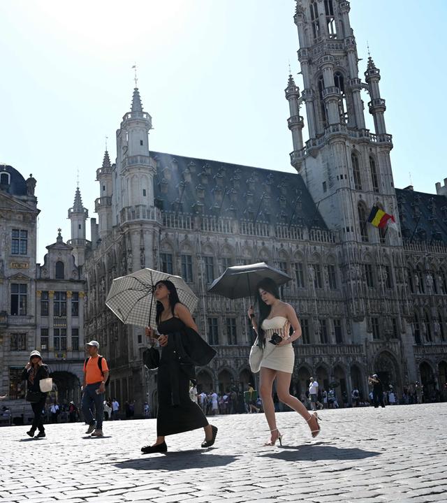 Touristen gehen während einer Hitzewelle in Brüssel mit Sonnenschirmen über den Grand-Place.